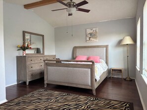 A bedroom with a bed, dresser, mirror, ceiling fan, artwork, lamp, and zebra-patterned rug. - Spacious home in Cedar Park w/ treehouse room. Pet-Friendly! (Cedar Park)