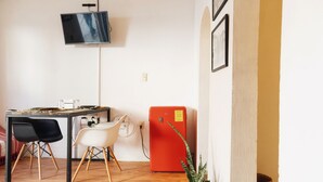 Una habitación con suelo de madera, una mesa con sillas, un televisor fijado a la pared y un electrodoméstico rojo.