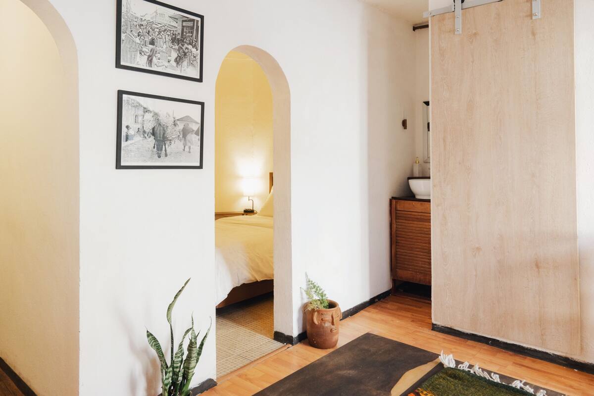 A room with a bed, a wooden cabinet, a potted plant, and two framed pictures on the wall.