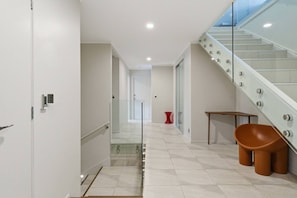 A modern hallway with a glass staircase, a red stool, and a brown chair. - Spacious 4BR Birkenhead Retreat | 3 Living Areas (Auckland North Shore)