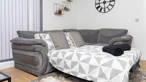 Een moderne woonkamer met een grijze bank, een decoratief plaid en wandplanken.