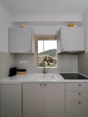 A kitchen with a window, white cabinets, a sink, and a stove. - Central sunset view #2 (Himarë)