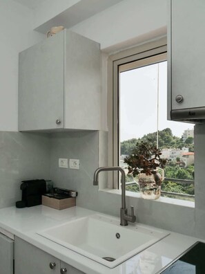 A modern kitchen with a white countertop, a built-in sink, and a window with a view of the city. - Central sunset view #2 (Himarë)