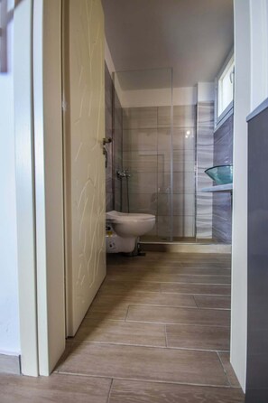 A bathroom with a toilet, shower, and glass-enclosed sink.