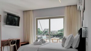 A hotel room with a bed, a desk, a chair, a TV, and a window with a view of buildings. - Central sunset view #1 (Himarë)
