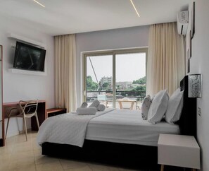 A hotel room with a bed, a desk, a chair, a TV, and a window with a view of buildings. - Central sunset view #1 (Himarë)