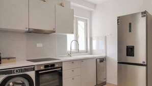 A compact kitchen with a washing machine, oven, dishwasher, and a stainless steel refrigerator. - Central sunset view #1 (Himarë)