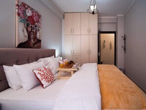 Habitación de hotel con cama, mesita de noche con desayuno, armario y un cuadro en la pared.
