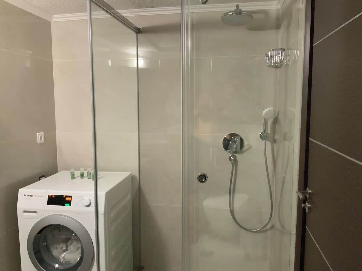 A compact bathroom with a glass-enclosed shower, a washing machine, and a toilet.