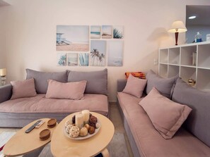 Un salón moderno con dos sofás grises, una mesita de centro con adornos, y obras de arte en la pared que muestran escenas de playa.