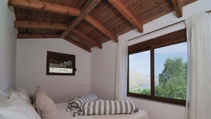 A bedroom with a wooden ceiling, a bed with white bedding, a window with a view of greenery, and a framed picture on the wall. - Ionian Manor Estate villa (Porto Palermo)