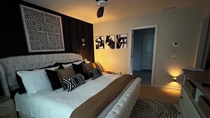 Un dormitorio con una cama, ventilador de techo, una puerta y una pared con diseño geométrico.