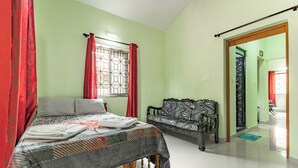 Un dormitorio con cama, sofá, ventana con cortinas y puerta que da a otra habitación.