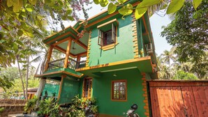 Una casa de dos pisos con un balcón, un portón de madera y macetas con plantas.