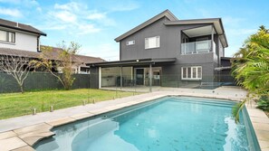 Una casa moderna de dos plantas con piscina, un porche cubierto y patio trasero cercado.