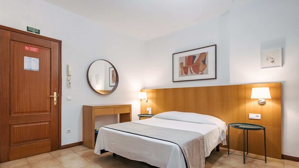 A hotel room with a bed, bedside tables, a mirror, and a framed picture on the wall. - Economy Studio Apartment in the heart of Funchal. 2' walk from Cathedral. (Funchal)