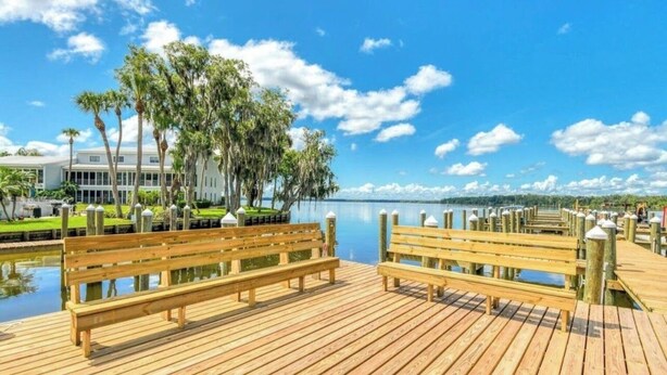 Eine Holzstege mit Bänken, ein ruhiger See und ein Gebäude mit weißer Fassade.