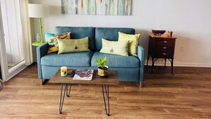 Ein Wohnzimmer mit blauem Sofa, Couchtisch, Lampe und einem Gemälde an der Wand.