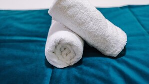 Ein Bett mit einer türkisblauen Bettdecke und zwei aufgerollten weißen Handtüchern darauf.