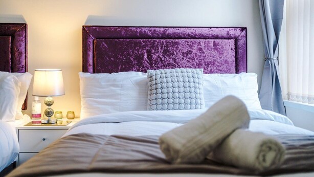 Ein Hotelzimmer mit einem großen Bett, einem Nachttisch mit Lampe und einem Fenster mit Vorhängen.
