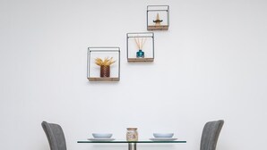 Ein Essbereich mit zwei grau gepolsterten Sesseln, einem Tisch mit Glasplatte und drei gerahmten Wanddekorationen.