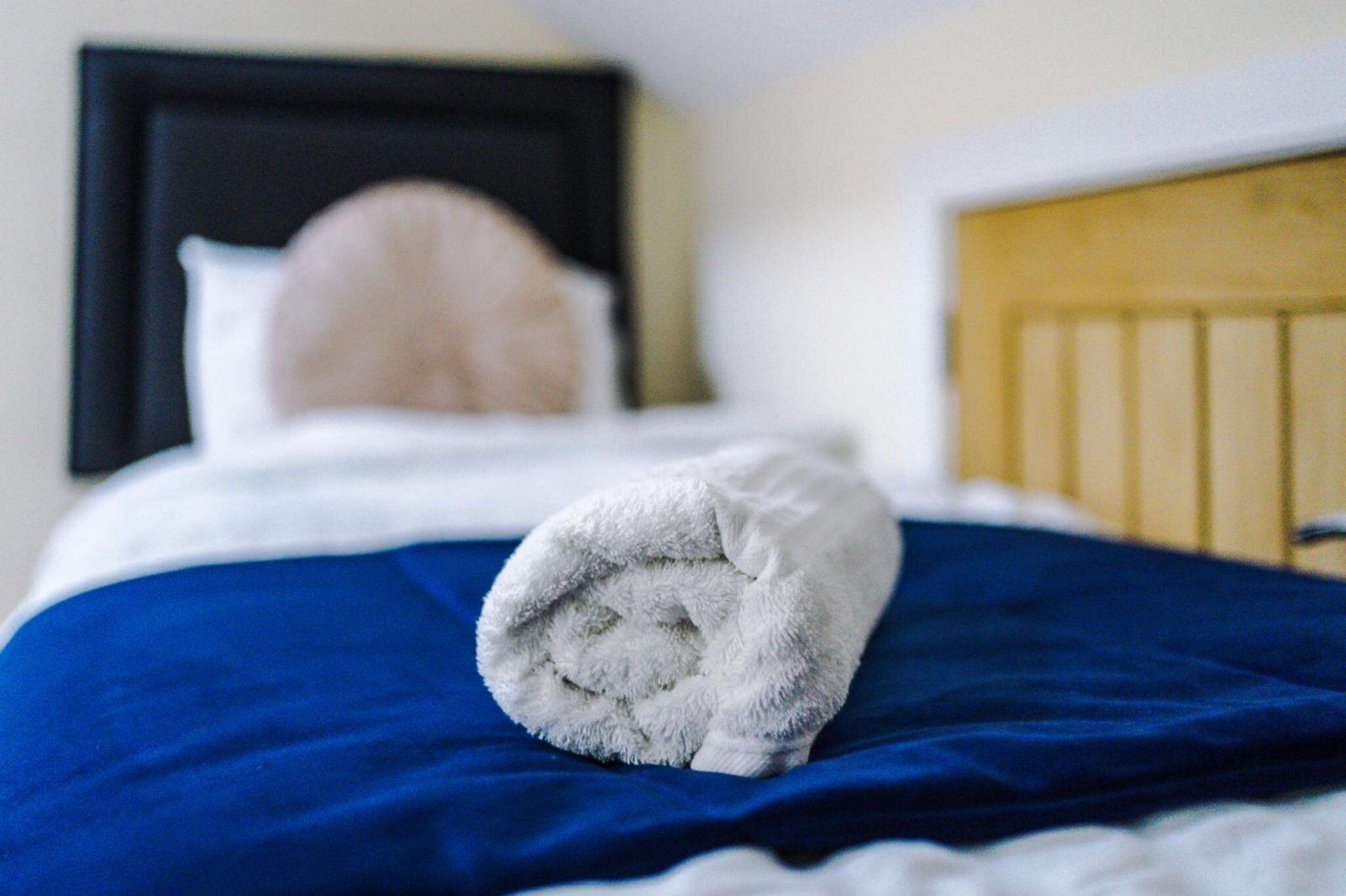 Un lit bien fait, avec une couvre-lit bleue et une serviette blanche pliée posée sur le dessus.