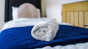 Ein ordentlich bezogenes Bett mit einer blauen Bettdecke und einem auf dem Bett drapierten weißen Handtuch.