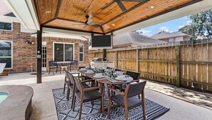 Une terrasse extérieure dotée d’un plafond en bois, d’une piscine, d’une table à manger pour six personnes et, au fond, d’une clôture en bois.