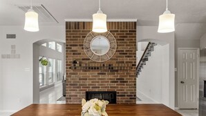 Un coin repas agrémenté d’une cheminée en briques, d’un grand miroir rond et de luminaires suspendus.