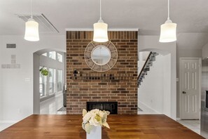 A dining area with a brick fireplace, a round mirror, and hanging pendant lights.