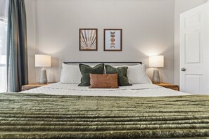 A neatly arranged hotel room with a bed, two bedside lamps, a window with curtains, and two wall-mounted artworks.