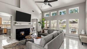 Un salon avec une cheminée, un grand canapé, un téléviseur et un ventilateur de plafond.