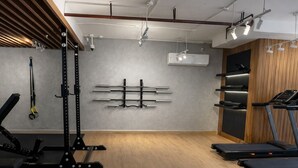 Un gimnasio con equipo de ejercicio, piso de madera y pared gris.