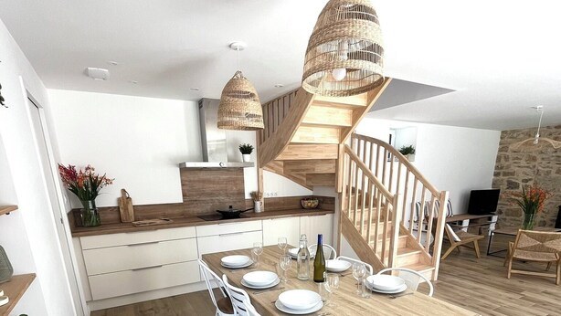Una cocina moderna con una isla central, sillas blancas y una mesa de comedor de madera.