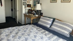 A bedroom with a bed, a desk, and a chair. There are framed pictures on the wall.