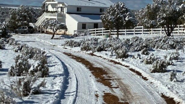 A snow-covered landscape with a white house, a dirt road, and a white fence.