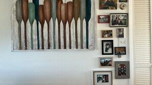 A wall with a wooden paddle painting and several framed photographs.
