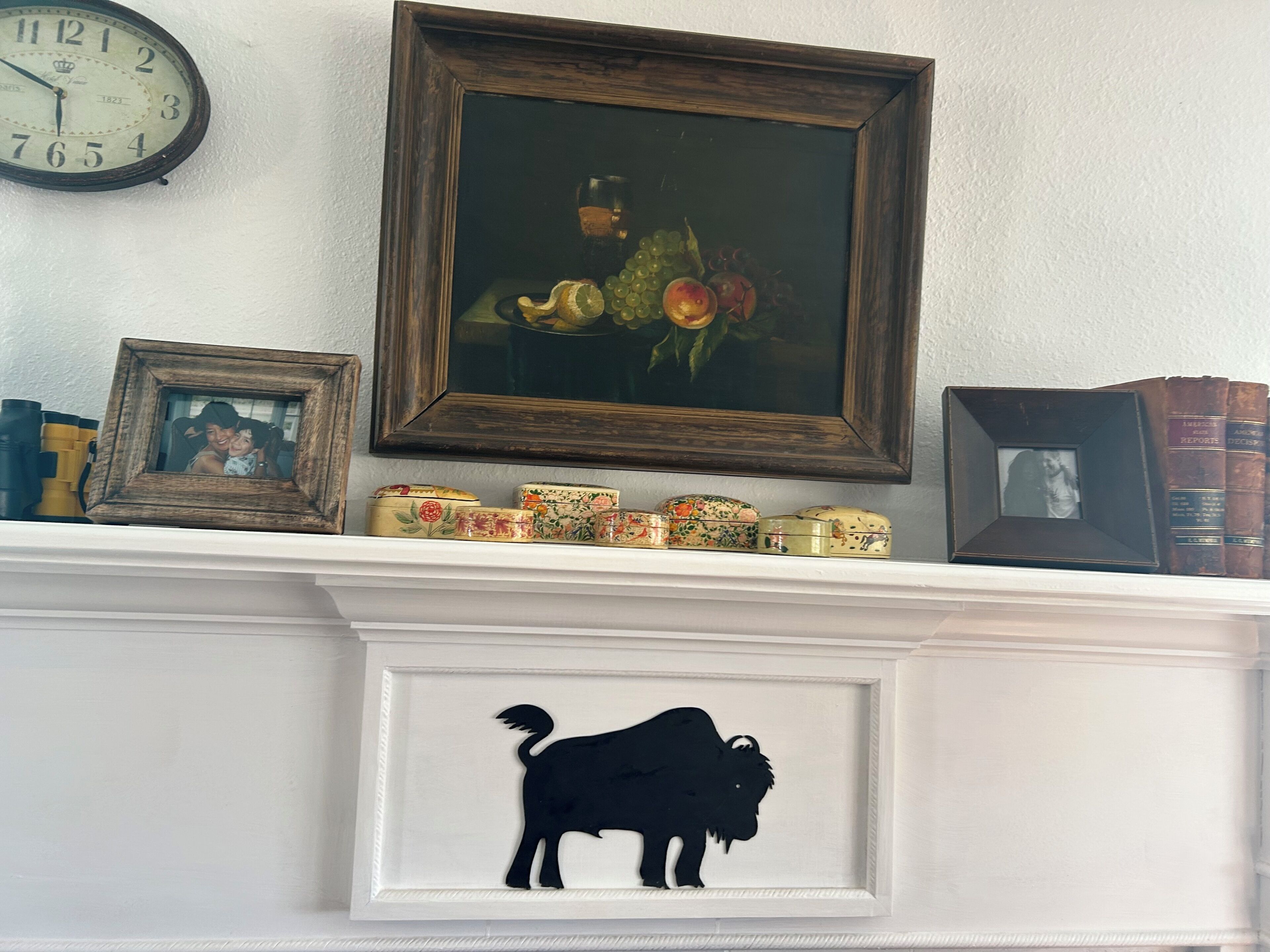 A fireplace mantel with a framed painting, a clock, and decorative items.