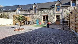 Un bâtiment en pierre avec une allée en gravier, un petit palmier et du mobilier d’extérieur.