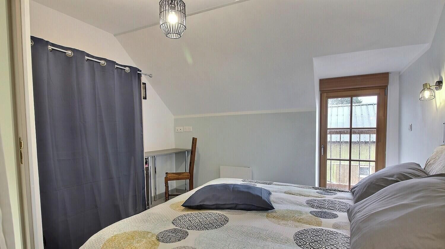 A bedroom with a bed, a chair, a desk, a window, and a curtain.