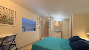 Een slaapkamer met een bed, een bureau, een stoel, een douche en een badkamer.