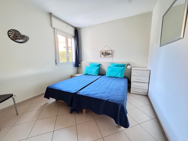 Un dormitorio con cama, mesita de noche, una silla, ventana y un adorno en la pared.