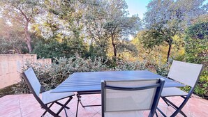 Een terras buiten met een metalen tafel en stoelen, omgeven door groen en bomen.