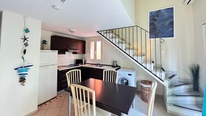Een moderne keuken met donkere kastjes, een zwart aanrecht en een eethoek met tafel en stoelen.