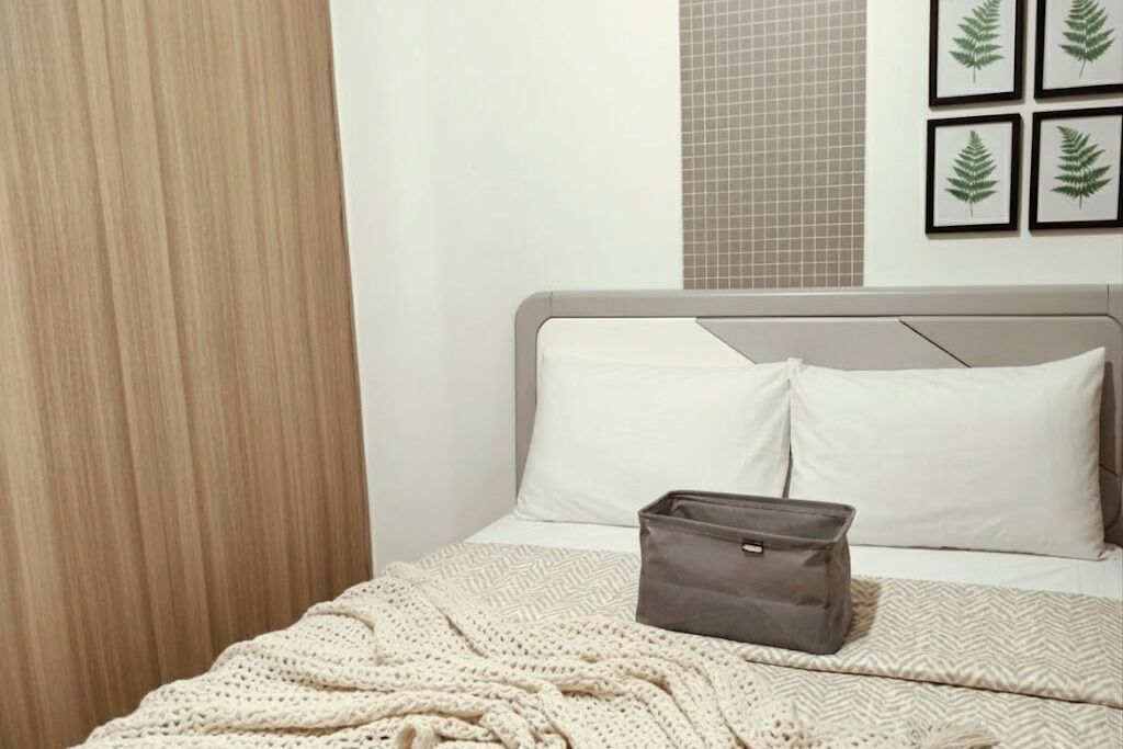 Un dormitorio con cama, almohadas, una colcha, un bolso de mano y cuadros en la pared.