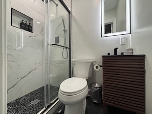 A modern bathroom with a glass shower enclosure, a white toilet, and a wooden vanity. - Welcoming 1-bedroom apartment in Washington DC. Free Parking Pass (Washington)