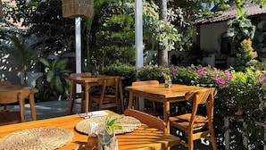 An outdoor dining area with wooden tables and chairs, woven hanging lights, and lush greenery. - White Coconut Resort (Gili Trawangan)