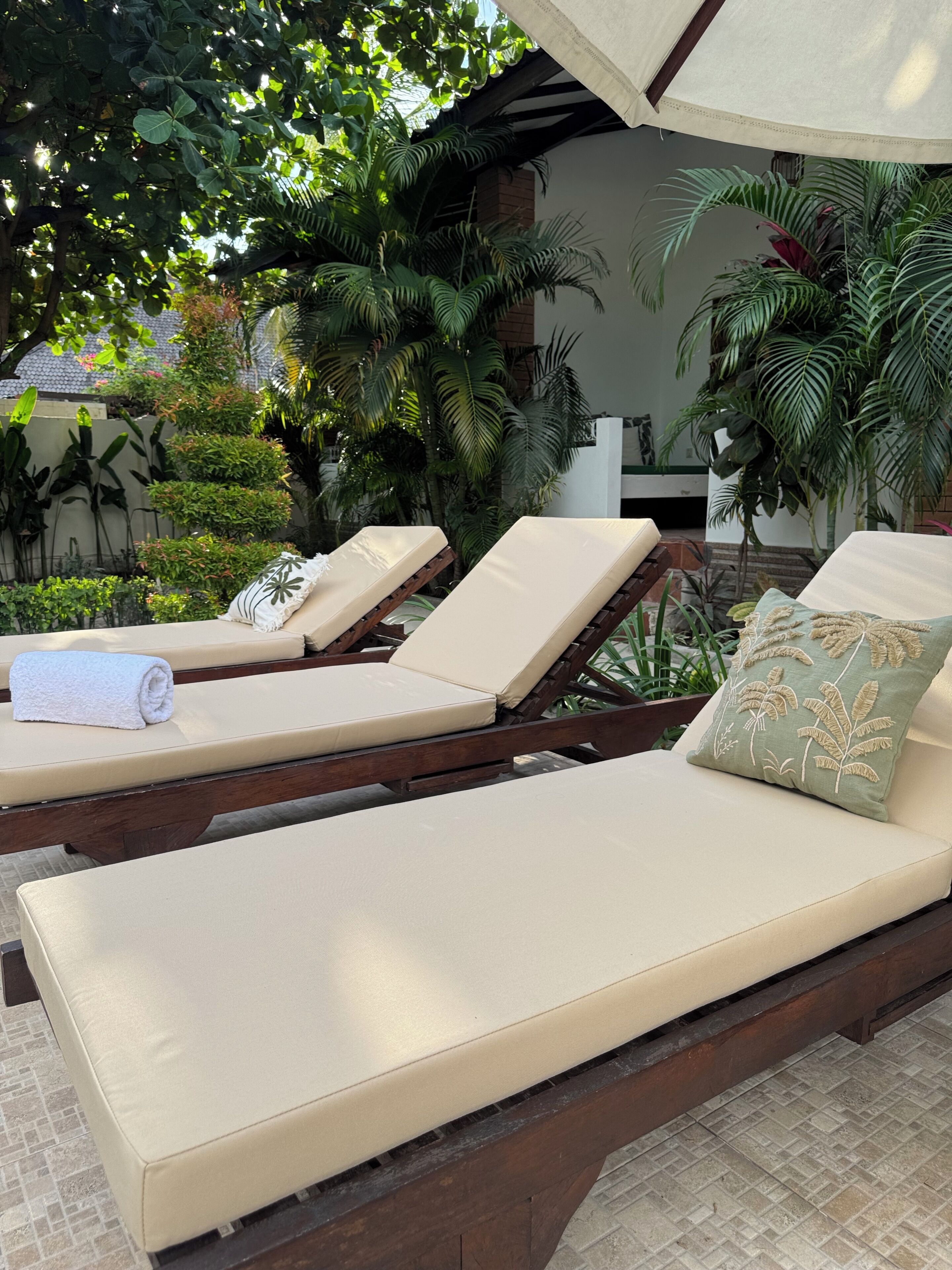 Uma área de estar à beira da piscina com espreguiçadeiras, chão ladrilhado e exuberantes plantas tropicais.