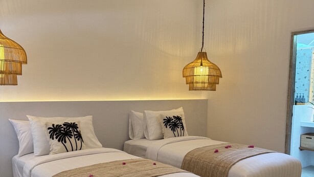 A bedroom with two beds, a hanging light fixture, and a window. - White Coconut Resort (Gili Trawangan)