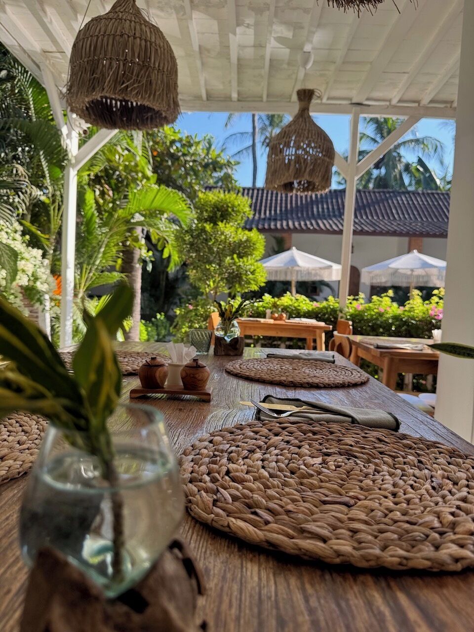 An outdoor dining area with woven placemats, a wooden table, and a hanging light fixture.